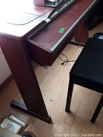Side view of brown wood digital piano console with matching bench