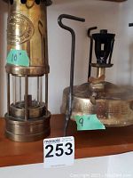 Overall photo showing both pieces of the brass lantern: the fuel chamber cylinder and the fuel tank base with burner, each individually measured with blue tape labels.