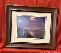 Framed photograph shows the Golden Gate Bridge at night with illumination over water, surrounded by a double mat and brown wooden frame.