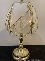 Lamp base and glass shade front view showing brass base and wire framing with decorative glass panels.