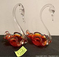 Pair of vintage handcrafted glass swans with orange-red bowl bases and clear necks shaped as swans on black surface