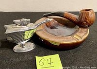 Photo of vintage metal lighter shaped like a bird and brown ceramic ashtray with pipe design.