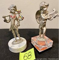 Two antique metal figurines: a young man with a flag on marble base and a cherub playing a lyre on a clear base with an orange sphere inside