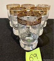 Front view showing the six matching glasses arranged in a group, highlighting the thick heavy bases, clear glass, and ornate gold rim.