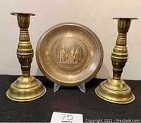 Full view of two brass candle holders and one brass plate with Egyptian engravings