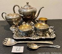 Full silver plated tea set including teapot, creamer, sugar bowl, small bowl, serving tray, and two serving utensils shown together on a table.