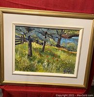 Full frontal view of framed landscape oil painting featuring grassy meadow, trees and river