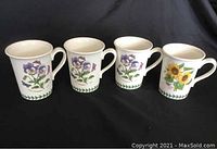 Four Portmeirion Botanic Garden coffee mugs with botanical flower illustrations and green vine border, shown against black background.