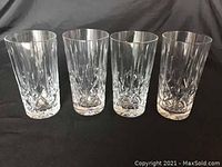 Front view of four faceted clear crystal glasses arranged in a row on black background.