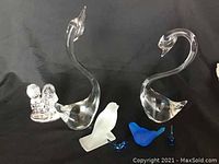 Pair of clear glass swans, frosted and cobalt blue birds, and Precious Moments crystal figurine shown together on black background.
