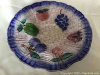 Top-down view of the large glass fruit bowl showing painted fruit designs and textured glass with cobalt blue scalloped rim.
