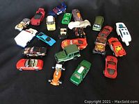 Top-down view of 23 assorted toy cars arranged on black fabric, showing the variety in size, color, and model types.