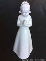 Front view of the white porcelain figurine of a praying girl, showing her head bowed and hands clasped.
