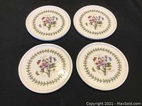 Four round ceramic coasters with botanical floral design and green leaf border arranged on black surface.