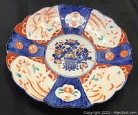 Top view showing full decorated surface of scalloped porcelain plate with floral and geometric patterns in blue, red, green, and cream enamel.