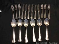 Full set of forks, knives, and spoons laid out in rows on black cloth background