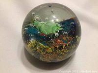 Clear spherical glass paperweight with internal sea creature sculpture and colorful seaweed-like inclusions seen from above.