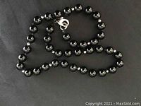 Close-up of black round polished jade bead necklace with lobster clasp on black background.