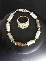Jade bracelet with carved jade beads and sterling silver clasp, alongside silver-tone ring with green stones.