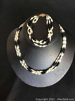 Photo of necklace and matching bracelet on a black display stand showing triple strands of fresh water pearls and black beads with a decorative clasp.