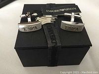 Pair of rectangular sterling silver Emporio Armani cufflinks with engraved logo, displayed on original black box with branded ribbon and booklet.