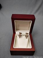 Pair of medium-sized hoop earrings displayed in a reddish wooden jewelry box with cream-colored interior.