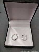 Pair of hammered style 14k gold hoop earrings displayed open in a jewelry box with white interior lining.