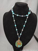 Front view of blue beaded cloisonné necklace with floral pendant displayed on black necklace bust.