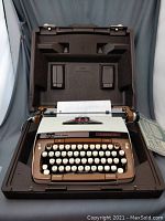 Front view of the typewriter in its open carrying case showing the keyboard and paper feed roller.