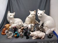 Full lot of feline figures showing mostly white ceramic cats and smaller painted wooden and ceramic cats.