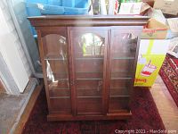 Full view of the small wooden curio cabinet showing three glass doors and glass shelves inside.