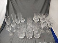 Full lot of crystal glassware arranged on grey fabric, showing multiple stems and glass types with pinwheel patterns.
