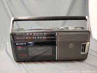 Front view showing Sony branding, AM/FM frequency scale, cassette window, and speaker.