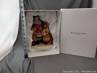 Side view with the figurine still in original white box lined with satin-like fabric and a measuring tape showing height about 8 inches.