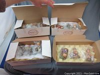 Four boxes each containing multiple wrapped vintage Hummel Christmas-themed figurines on cushioning foam inside, mostly children and holiday characters.