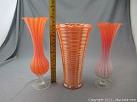 Photo showing three orange vases of varying shapes next to a ruler for size reference, demonstrating height and design details.