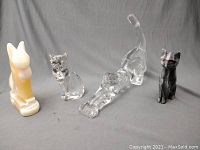 Lot of four cat figurines displayed together on a grey background, showing different materials and shapes