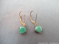 Pair of leverback dangle earrings with cloudy green quartz stones in four-prong settings on a gray surface.