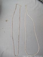 Two different silver chains laid out, one beaded and one flat snake design.
