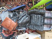 Suitcase open showing multiple women's purses in black, brown, and tan colors along with a black puffer jacket inside.
