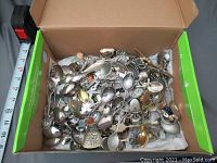 Top-down photo of large assortment of spoons in cardboard box showing many items piled together.