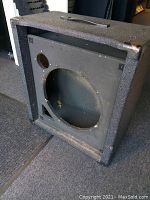 Full view of Peavey KB-100 empty cabinet showing black textured surface, front panel with large circular cutout for speaker, and handle on top