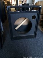 Front view of black speaker cabinet with large circular cutout and smaller round port hole, showing overall condition.