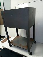 Full side view of gray metal rolling file cabinet showing bent lower shelf, oxidation on bottom shelf, castors and exterior surface.