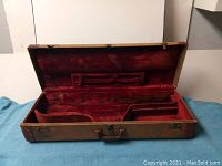 Open vintage tenor saxophone case showing reddish velvet interior with two compartments and rod reinforcement cushion.