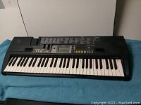 Full view of the Casio CTK-710 keyboard showing all 61 keys, control panel with LCD display and buttons, and speaker grilles. The keyboard is black and laid on a blue surface.