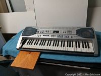 Front view of the Casio LK 90TU lighting keyboard showing the damaged keys, control panel, speakers, and the wood board extending from the rear panel.