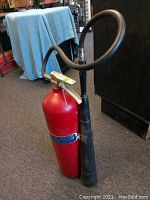 Front view of the vintage red General Model 15RH fire extinguisher showing the cylinder, operating handle, chain, and black rubber hose with tapered nozzle.