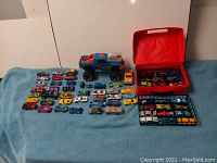 Wide view of the 62 toy cars, including two red storage cases with miniature cars, and the large blue and orange Slate Raptor toy vehicle with raised engine and orange frame on wheels.
