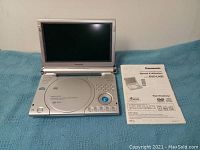 Panasonic portable DVD player opened with screen up, placed on a blue textured surface next to its instruction manual.